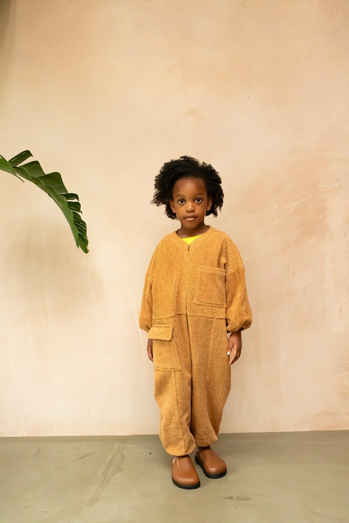 The Rae Boiler Suit is a fresh take on your favourite overalls. Made from a soft, organic cotton teddy fleece in a warm caramel tone, this boiler suit is perfect for keeping little ones snug during cooler days. The Teddy Boiler Suit has an oversized fit with elasticated cuffs, patch pockets and a zip front, it has been designed for easy dressing and functionality. The unisex design makes it versatile, ideal for layering and everyday wear. Key Features: Made from 100% organic cotton teddy Unisex design Zip front for easy dressing Adjustable back, allowing a fit closer to the body Spacious pockets for storing tiny treasures Ideal for layering in cooler weather Studio Koter is a modern, unisex, functional kidswear shop designed in the UK and made sustainably in the UK and Portugal.