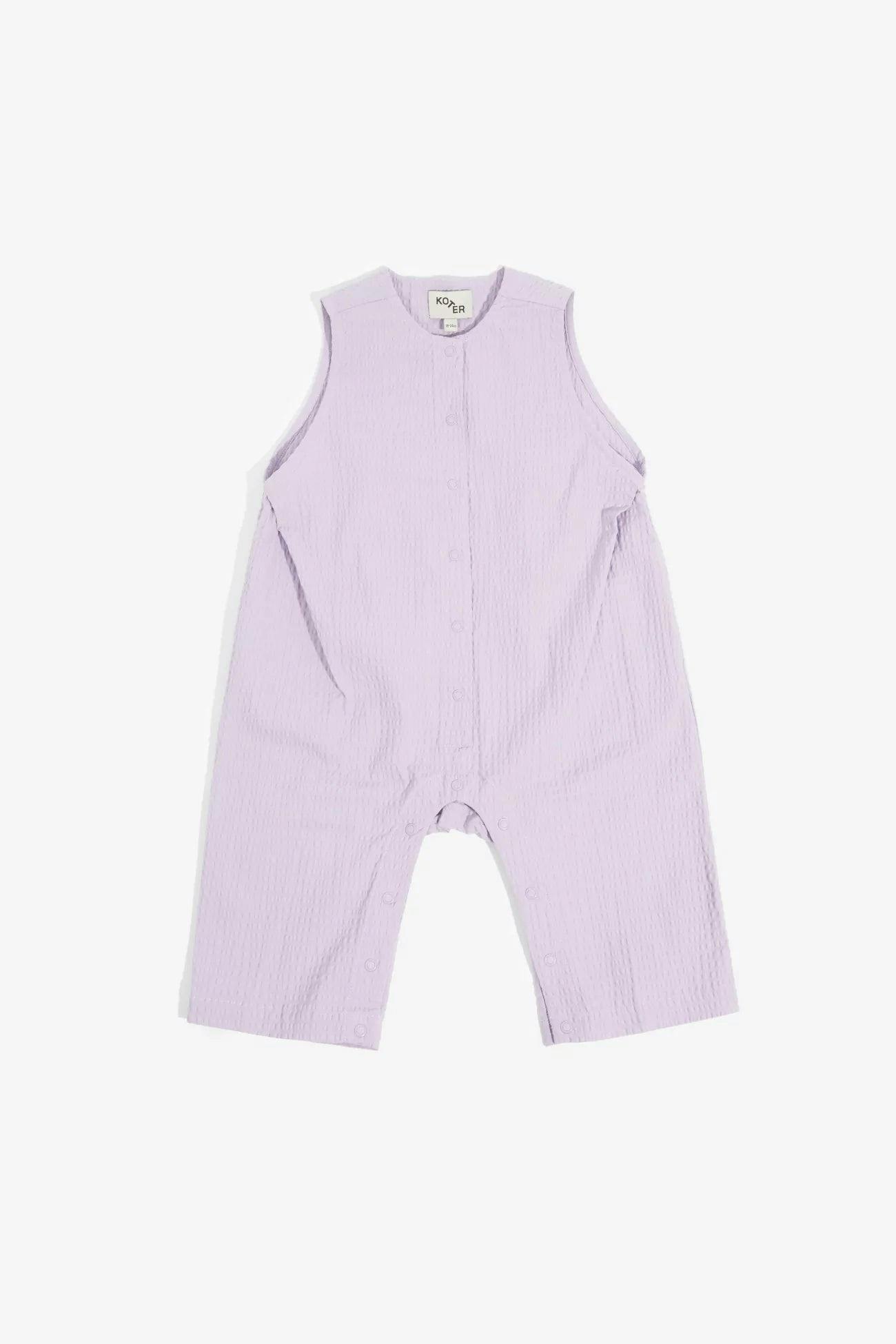 Playsuit in textured cotton, to wear on its own on warmer days or to layer with our Rory t-shirt. Yoke and curved seam-detail in back, subtle pleats to create a new volume. Poppers in front and under the legs for easy access. The perfect, unisex summer playsuit.97% organic cotton 3% elastane (lilac seersucker)99% organic cotton 1% elastane (black)